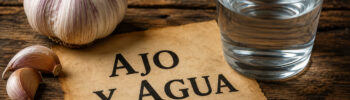 Выражение «Ajo y agua» на фоне чеснока и стакана воды